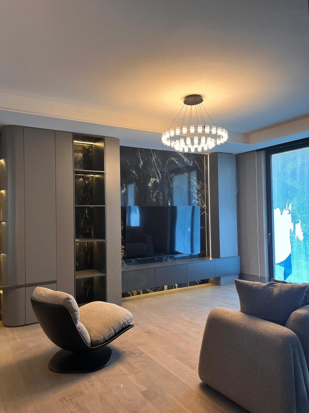 Salonda mermer desenli TV duvarı, gri lake kitaplık ve halka avize